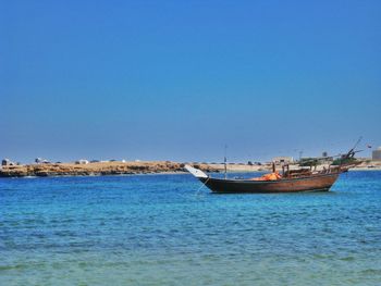 Boats in calm sea against clear sky