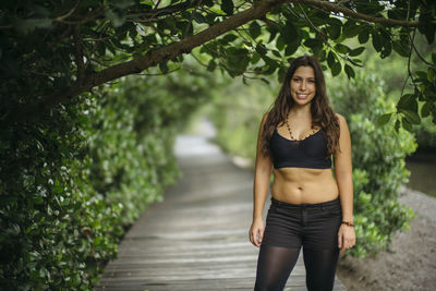 Portrait of young woman standing on boardwalk amidst plants