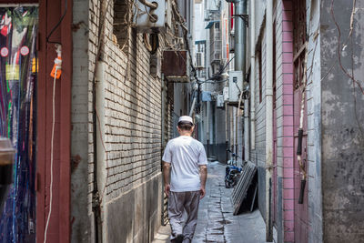 Rear view of man standing on alley amidst buildings