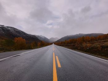 Empty road leading to mountains against cloudy sky