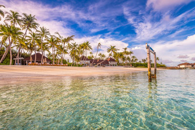 Scenic view of white sand beach in maldives with turquoise pristine water and dramatic sky