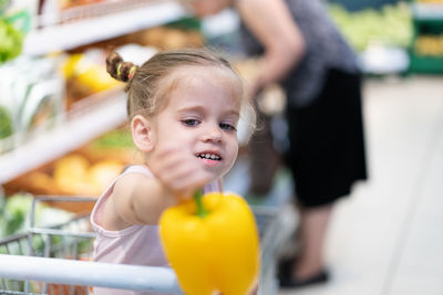 Cute girl holding yellow bell pepper at supermarket