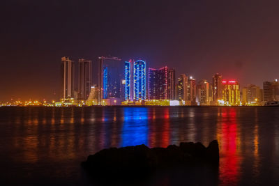 Illuminated city by river against sky at night