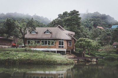 House and trees by lake against sky