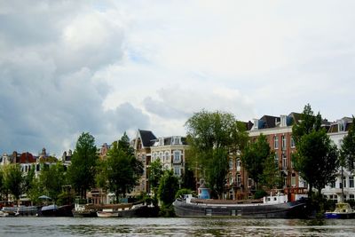 Boats moored in river by buildings against sky