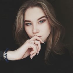 Close-up portrait of beautiful young woman against black background