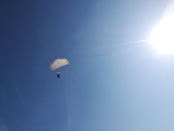 Low angle view of people paragliding against blue sky