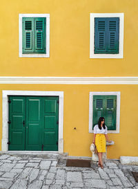 Full length of woman standing against yellow building