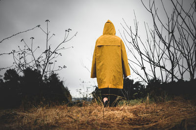 Girl in a yellow raincoat on a cloudy rainy walks between the trees. concept of loneliness