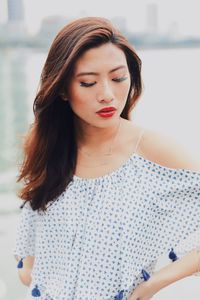 Young woman looking down while standing against river in city