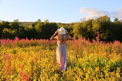 Rear view of woman wearing hat standing by flowering plants on field