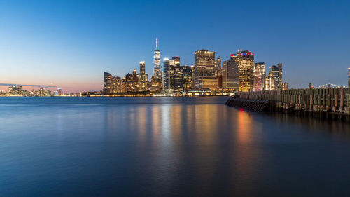 Illuminated new york city skyline against clear sky from governors island pier