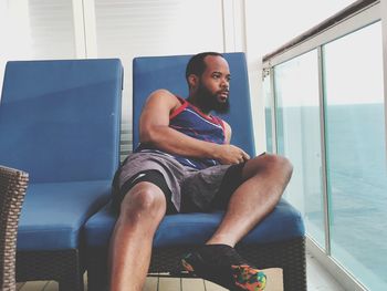 Mid adult man looking through window while relaxing on deck chair in ship