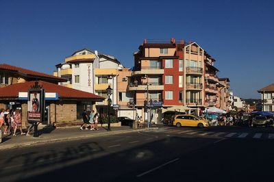 Cars on road by buildings against clear sky