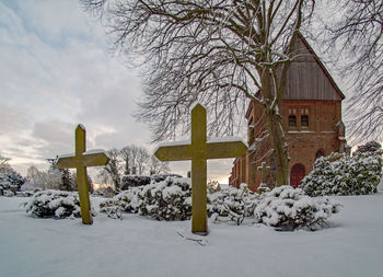 Cross on snow covered tree by building during winter