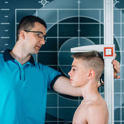 Man measuring shirtless male athlete height in health club