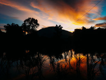 Silhouette trees by lake against sky during sunset