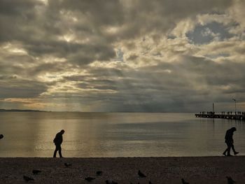 Silhouette people walking on beach at sea against sky during sunset