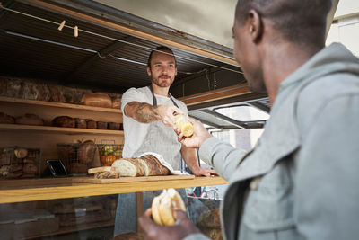 Young salesman giving bottle to male customer at food truck