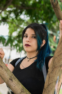 Latin college girl with blue hair walking through the park dressed in black and blue bag, surrounded