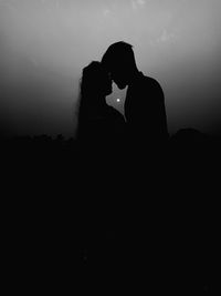Silhouette couple embracing while standing against sky at night