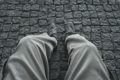 Low section of man sitting on cobblestone footpath