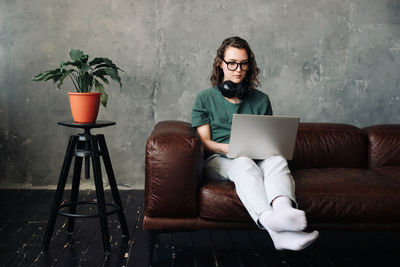 Young woman using laptop while sitting on sofa at home