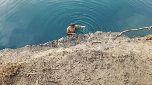 High angle view of shirtless man standing in lake by rock formation