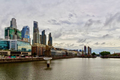 Buildings by river against cloudy sky