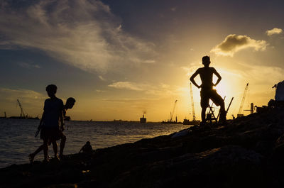 Silhouette men standing on beach against sky during sunset