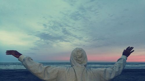 Close-up of hand on beach against sky during sunset