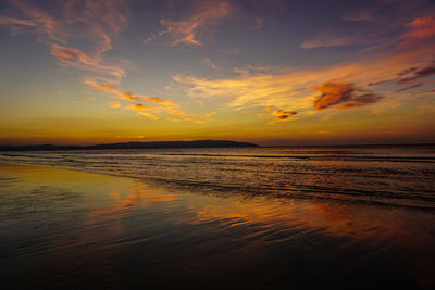 Scenic view of beach against sky at sunset