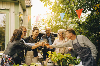 Active senior male and female friends with celebratory toast at back yard during garden dinner party