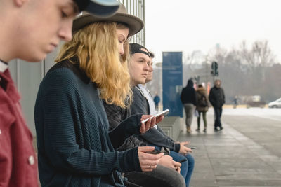 Side view of people sitting on footpath in city