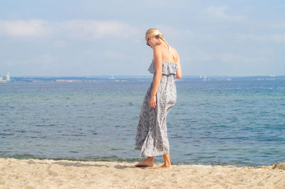 Full length of young woman standing on shore against sky