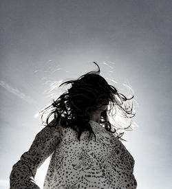 Low angle view of girl with tousled hair standing against sky