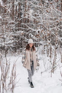 A cute girl in a coat and hat walks in a snowy forest along a path