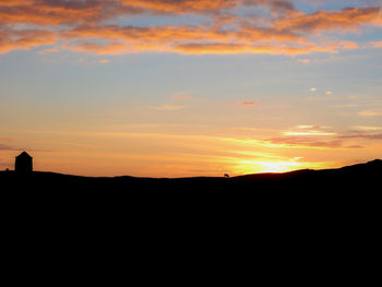 Silhouette landscape against orange sky