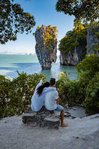 Rear view of woman sitting on rock by sea