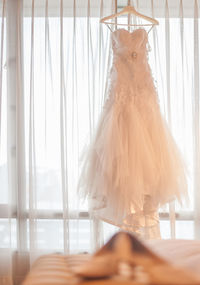 Close-up of wedding dress hanging against curtain