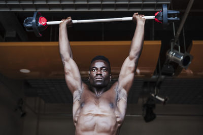 Confident muscular sportsman exercising with barbell in gym