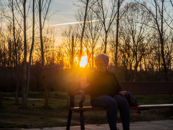 Senior woman sitting on bench in park during sunset