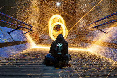 Woman wearing hoodie sitting on footbridge against light painting