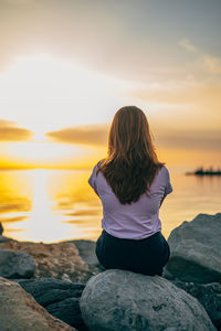 Rear view of woman looking at sea against sky during sunset