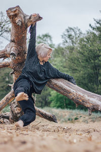 Full length of woman standing on fallen tree at forest