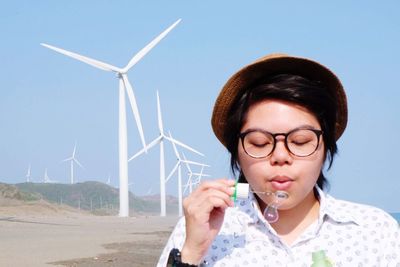 Young woman blowing bubbles against wind turbines
