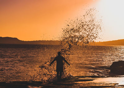 Man standing at beach against sky during sunset