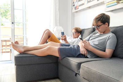 Brothers using mobile phone on sofa at home