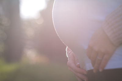 Midsection of pregnant woman standing outdoors during sunny day