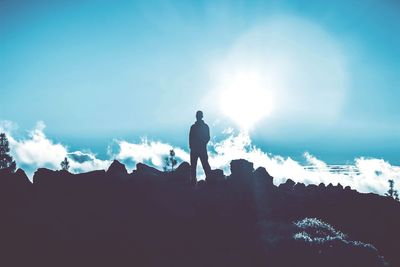 Rear view of silhouette man standing on rock against sky